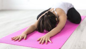 moteris atliekanti jogos pratimus namuose ant kilimėlio
